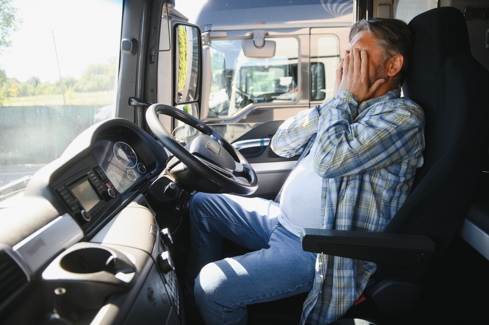 Tired, drowsy truck driver rubbing his eyes behind the wheel